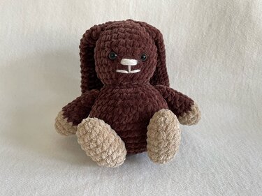 Brauner gehäkelter Amigurumi-Hase mit langen Schlappohren und beigen Pfoten auf hellem Hintergrund