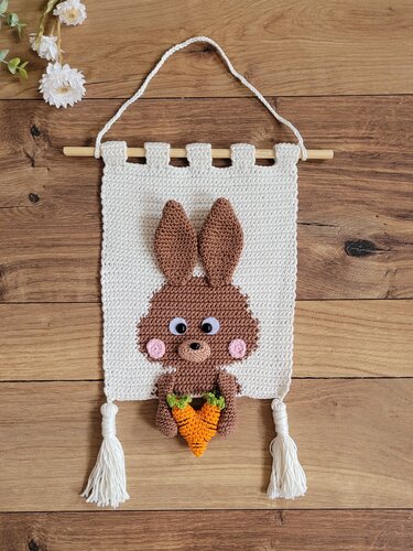 Gehäkelter Wandbehang in Creme mit braunem Hasenmotiv und Möhre, verziert mit weißen Quasten.