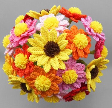 Round crochet bouquet of yellow, orange, pink and red yarn flowers with pom-pom centers