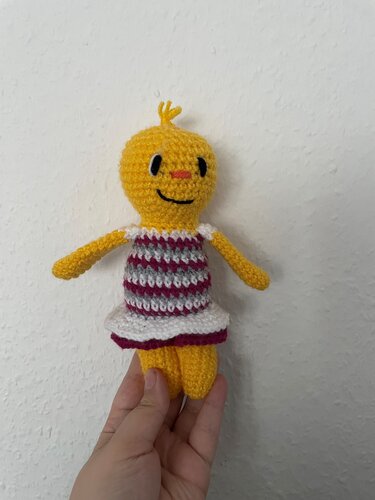 Gehäkeltes gelbes Amigurumi-Küken im gestreiften Kleid, in der Hand gehalten