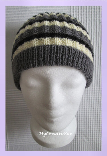 Gestrickte Beanie in Grau und Creme mit Rippenbund auf weißem Schaufensterkopf