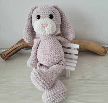 Zartrosa gehäkelter Amigurumi‑Hase aus flauschigem Chenille‑Garn auf weißer Miniaturbank