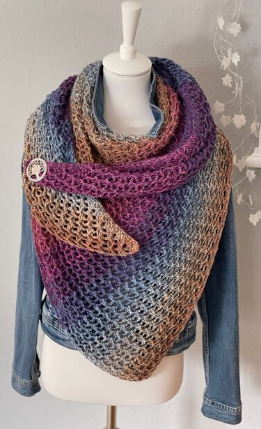 Gehäkeltes mehrfarbiges Dreieckstuch mit offenem Maschenbild, auf Schaufensterpuppe über Jeansjacke drapiert, mit runder Anstecknadel