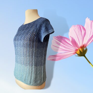 Gestricktes blau-türkises Kurzarmshirt auf Schneiderpuppe, daneben rosa Blume