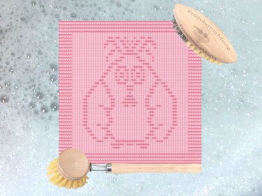 Rosa gestricktes Spültuch mit eingestricktem Kükenmotiv und Holzbürsten auf Seifenschaum