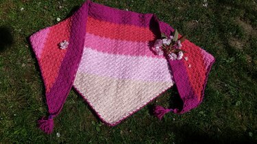 Gehäkeltes Dreieckstuch in Creme, Rosa und Magenta mit Quasten auf Gras liegend