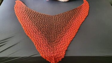 Gehäkeltes Dreieckstuch mit Muschelmuster und Ombre‑Farbverlauf von Braun zu Orange, auf dunklem Stoff ausgelegt
