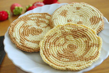 Drei runde gehäkelte Pfannkuchen mit zweifarbigen Spiralmustern auf weißem Teller.