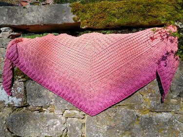 Gehäkeltes Dreieckstuch in Ombré von Pfirsich bis Rosa auf Natursteinmauer