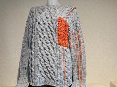 Light gray cable knit sweater with orange accents on a mannequin.