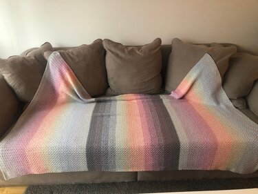 Gehäkelte gestreifte Decke in Pastell- und Grautönen auf braunem Sofa