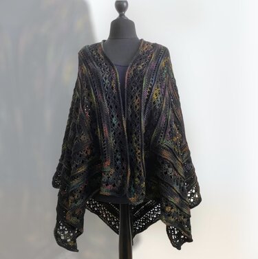 Dark crocheted shawl with openwork lace panels and subtle multicolor flecks on a mannequin.