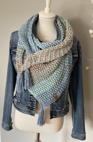 Gehäkeltes Dreieckstuch aus verlaufendem Blau-Beige-Garn mit Quasten und dekorativem Anker-Pin auf Schaufensterpuppe mit Jeansjacke