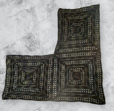 Dark L-shaped crocheted shawl of joined concentric square panels with light accent stitches