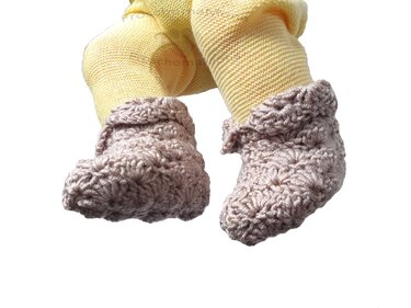 Gehäkelte rosa Babyschuhe an Babybeinen mit gelben Strumpfhosen