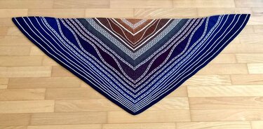 Gestricktes Dreieckstuch in Blau, Braun und Weiß mit Streifen- und Wellenmuster auf Holzboden