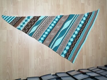 Gestricktes Dreieckstuch mit Rauten-, Wellen- und Zopfmuster in Türkis, Braun und Creme auf Holzboden
