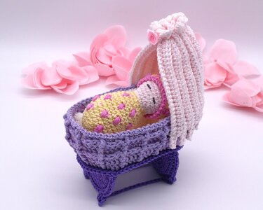 Gehäkelte Babypuppe in lila Wiege mit rosa Haube und gepunkteter Decke