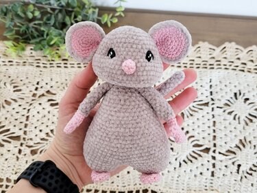 Gehäkelte Amigurumi‑Maus in Grau mit rosa Ohren, Nase und Pfötchen, handgehalten.