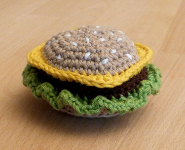 Handgehäkelter Burger-Spielzeug mit Brötchen, Käse, Patty und grüner Rüsche