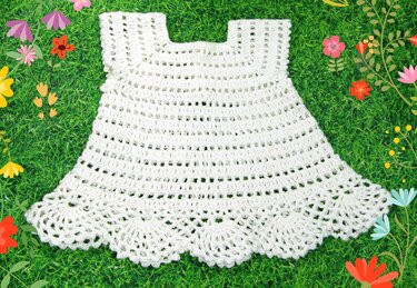 Weißes gehäkeltes Babykleid mit Muschelsaum auf grünem Rasen
