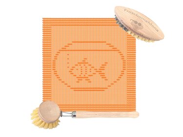 Quadratisches orangefarbenes Stricktuch mit Goldfisch‑im‑Glas‑Motiv und zwei Holz‑Bürsten daneben