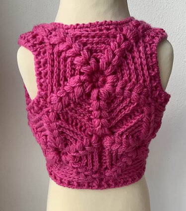 Rückenansicht einer leuchtend pinken, gehäkelten Kinderweste auf einer Schaufensterpuppe.