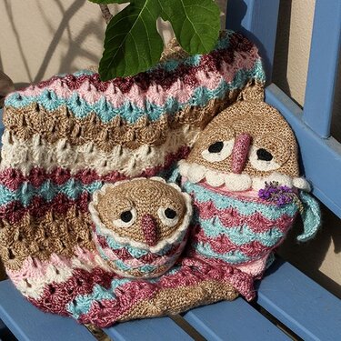 Gehäkelte Babydecke mit Zickzackmuster und zwei Eulen-Kuscheltieren in Pastellfarben