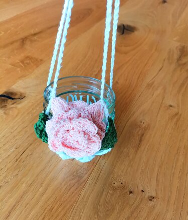 Glaswindlicht mit gehäkelter rosa Rose und grünen Blättern an weißem Band