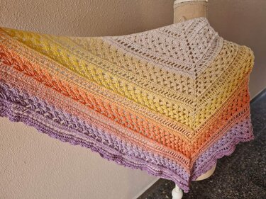 Gehäkeltes Dreieckstuch in Creme, Gelb, Orange und Lila mit feinem Lochmuster und gewellter Kante auf einer Schneiderpuppe drapiert.