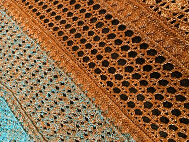 Close-up of openwork crocheted triangle shawl in orange-brown to blue-turquoise gradient