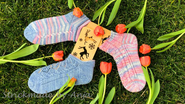Drei kurze gestrickte Socken mit Loch- und Streifenmustern auf Holzsockenblockern, umgeben von roten Tulpen auf Gras
