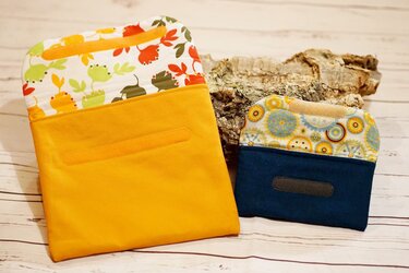 Gelbe Utensilo-Tasche und kleine blaue Stoff-Geldbörse mit gemusterter Klappe und Klettverschluss