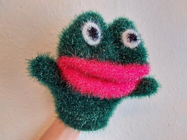 Grüne flauschige Frosch-Handpuppe mit pinkem Mund auf einer Hand