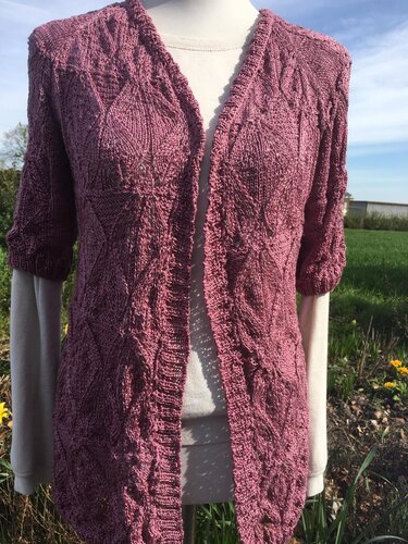 Altrosa gestrickte Damen-Kurzarmjacke auf einer Schaufensterpuppe vor grüner Kulisse