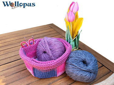 Gehäkelter pink-violetter Korb mit Wollknäueln und Schere auf Holztisch, Tulpen im Hintergrund