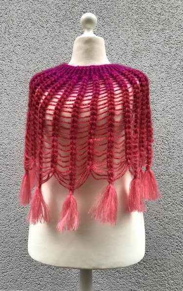 Damen‑Häkelponcho in Pink und Magenta mit Quasten auf Schaufensterpuppe