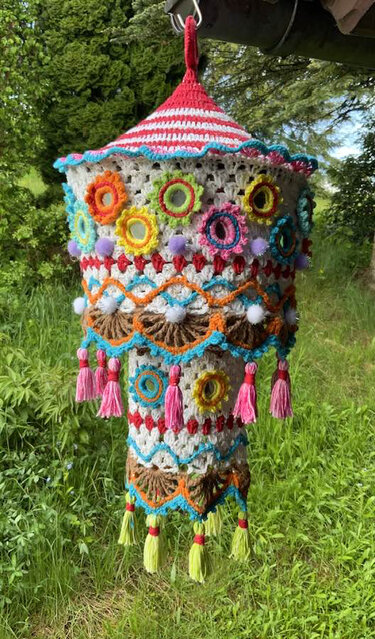 Handgearbeiteter, farbenfroher Häkel-Lampion mit floralen Mustern, Pompons und Quasten, im Grünen hängend