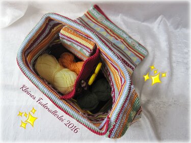 Draufsicht auf eine gestreifte, gehäkelte Umhängetasche mit Innentaschen, Garnknäueln und Häkelnadeln