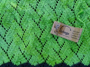 Nahaufnahme eines grünen gestrickten Schals mit Blattspitzen-Lochmuster und Papieretikett