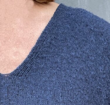 Nahaufnahme eines blauen, fein gestrickten Damenpullovers mit V-Ausschnitt