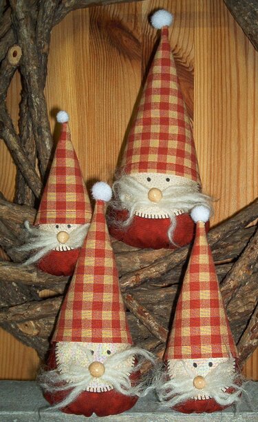 Vier genähte Weihnachtswichtel mit rot-beigen karierten Mützen, Holz-Nasen und weißen Bärten vor Holz