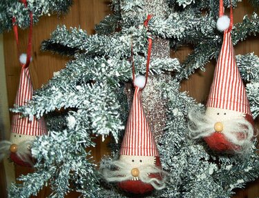 Detaillierte Ansicht von drei genähten Wichtel-Anhängern mit gestreiften Mützen und kleinen Nasen an einem verschneiten Weihnachtsbaum.