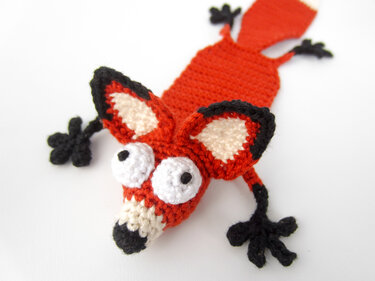 Crocheted orange fox bookmark with large white eyes and black details on a white background.