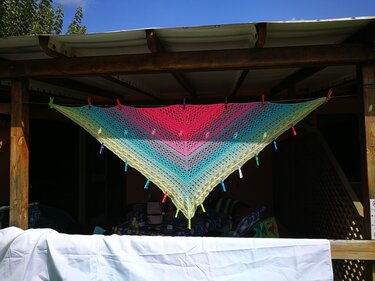 Gehäkeltes Dreieckstuch mit Farbverlauf von Pink über Blau zu Gelb, an einer Leine mit Wäscheklammern gespannt