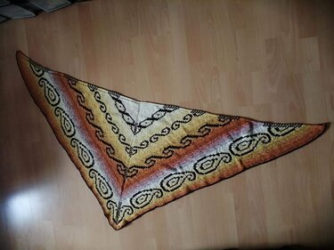 Gestricktes Dreieckstuch mit Creme‑bis‑Orange‑Braunem Farbverlauf und schwarzen Ornamentreihen auf Parkettboden.