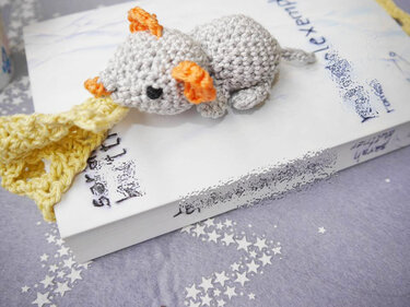 Gehäkeltes graues Mäuse-Lesezeichen mit orangen Ohren auf einer Buchseite