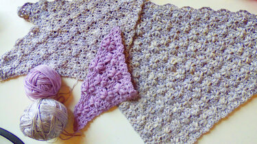 Gehäkelte Dreieckstücher in Hellgrau-meliert und Lila mit sternförmigem Puffstichmuster und zwei Garnknäueln