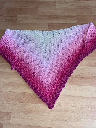 Gehäkeltes Dreieckstuch mit Creme- bis Magenta-Farbverlauf und Muschelmuster, auf Holzboden ausgebreitet