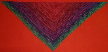 Gehäkeltes Dreieckstuch in Rot, Lila und Grün mit offenem Spitzenmuster auf rotem Hintergrund